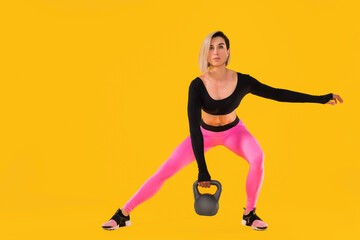 Fototapeta na wymiar Fitness woman in fashionable pink and black sportswear work out with kettlebell on yellow background. Strength and motivation.