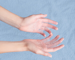 Hands of a young girl in the foam from the detergent, soap on the background of a soft blue towel. Personal hygiene, protection from bacteria during a pandemic. Skin care peeling. Photo close up