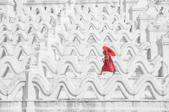 Novice monk carrying a parasol walking across a temple wall, Myanmar