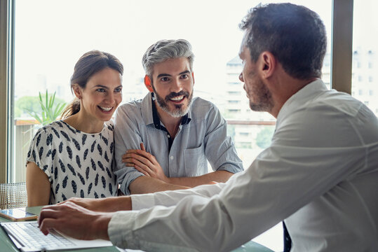 Happy couple looking at real estate agent in office