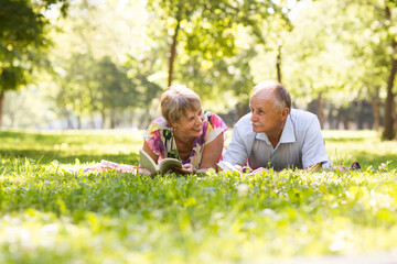 Naklejka na ściany i meble senior couple read books lying on the grass in the park