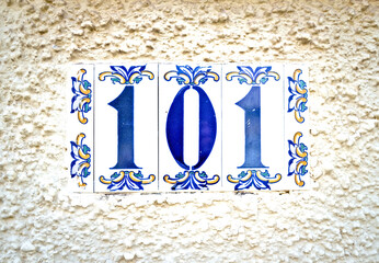 Number 101, one hundred and one, blue numerals on tiles on a pale vigneted background.