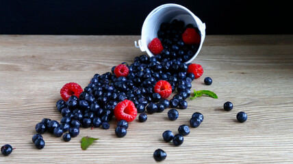 Bouquet of sweet and juicy blueberries, raspberries scattered from a bucket on a wooden background. The concept of healthy eating in the summer.