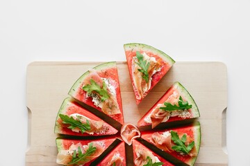 Slice of watermelon with prosciutto and rucola on wooden board