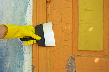 Worker's hand in a protective yellow glove cleans paint from a door with a spatula. Coating removal...