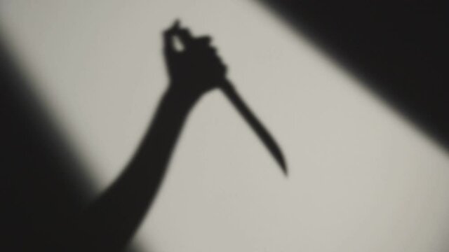 Hand of Killer Stabbing Victim with a Knife. Crime Scene. Dark Shadow on the White Background