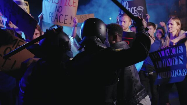 Vigorous interracial group of protesters striking by police borderline. USA police officers in duty suppress aggressive activists crowd at night on street. Stop racism concept.