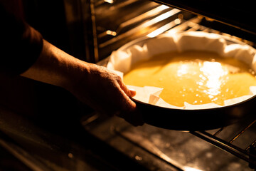 Female hands putting a bowl of raw dough from a homemade cake into the oven. Make a homemade cake at home in the kitchen at warm light.