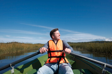 A young man in a life jacket sits in a boat, rowing oars