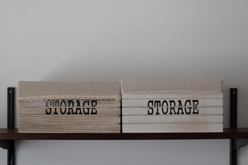 Wooden boxes on shelf with the word storage painted in black letters and lace decorative top border. White wall background with empty space for text. Organization and store concepts