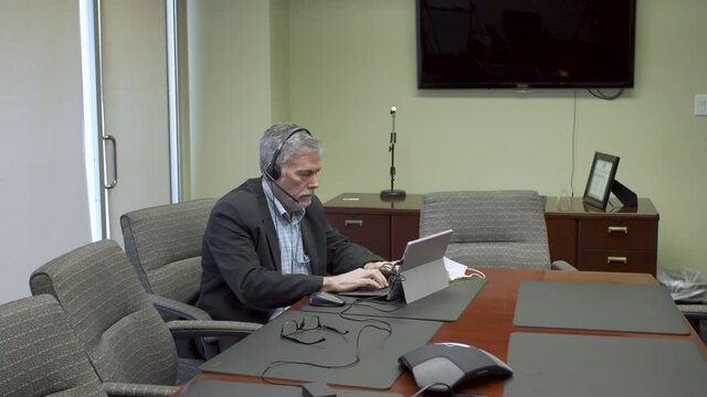 A businessman in a corporate board room having a web conference via a virtual meeting using a tablet pc.