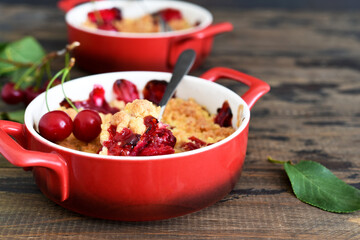 Homemade summer dessert with cherries. Crumble with cherries in a baking dish on a wooden background.