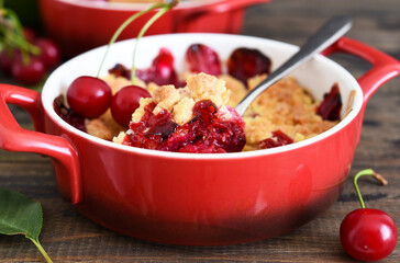 Homemade summer dessert with cherries. Crumble with cherries in a baking dish on a wooden background.
