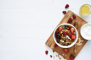 Classic breakfast - granola with honey, yogurt and berries on a white wooden background. View from above.