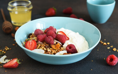 Classic breakfast - granola with honey, coconut, yogurt and berries on a black background.
