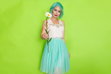 Studio portrait of beautiful mint hair feminine in white top and light blue skirt holding big chamomile in her hands,