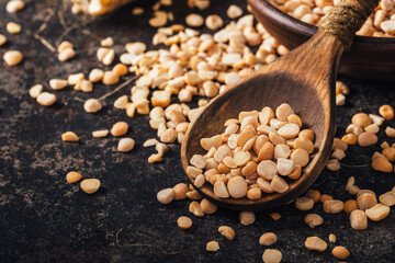 Pea seed in wooden spoon on dark background.