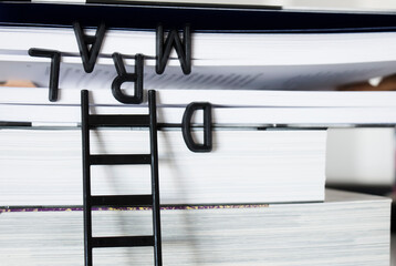 Plano frontal de un concepto abstracto donde letras de plásstico negro ingresan a las páginas de un libro de páginas blancas a través de una pequeña escalera
