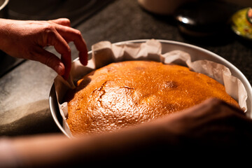 Woman preparing a delicious homemade cake just out of the oven with warm kitchen light. Freshly baked hot cake on top of the kitchen marble.