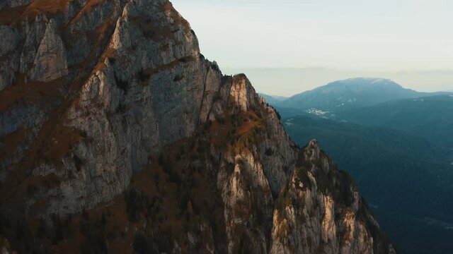 Aerial view on rocky peak mountains. Video from drone flying over valleys, forested and cliffs slopes of the mountain range. Sunset time in Romania, Majestic landscape, travel background, 4k