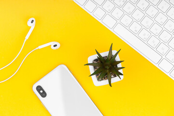 Smartphone, headphones and keyboard on yellow background.