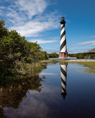 Cape Hatteras lighthouse and reflection in large pool of rain water with stunning blue sky and soft...