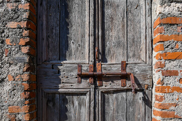 Close-up of an old wooden door ruined by time with a rusty lock and a brick wall, Italy