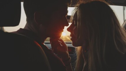 Portrait of young casual pretty lovers looking at each other with tenderness and sitting in car at sunset while long roadtrip. Moment before a romantic kiss. Concept of love and travelling
