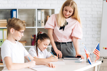School lesson. Pupils sit at their desk and complete school assignments, and the teacher helps...
