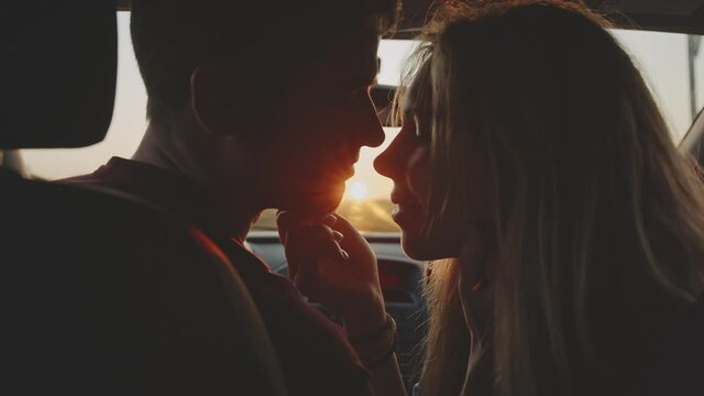 Portrait of young casual pretty lovers looking at each other with tenderness and sitting in car at sunset while long roadtrip. Moment before a romantic kiss. Concept of love and travelling