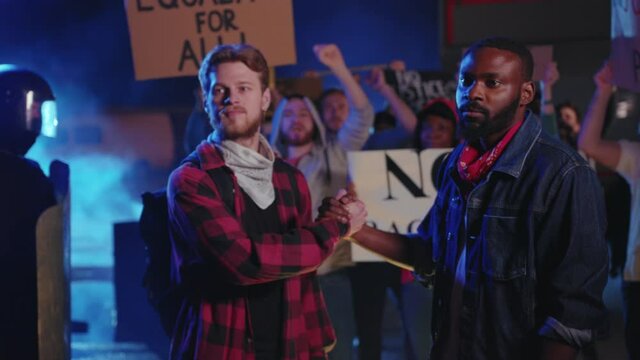 Diverse male couple of rally activists shaking hands to express friendship, cooperation, equality. Crowd of american people protesting for liberty. No racism concept.