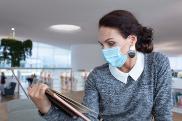 Woman, brunette, in a business setting, with a book, in a medical mask, protecting her health during coronavirus