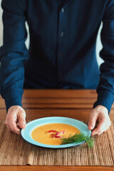 Tasty carrot cream in a blue plate served in a wooden table while a man is ready to eat.