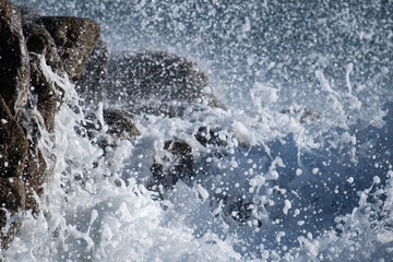 Water droplets in the air as white foamy waves crash against rocks on the ocean shore