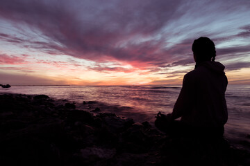 Silhouette of young woman wearing exercise clothes practicing yoga on the beach at sunset or sunrise. women do yoga. women exercising yoga in the beach.Young girl meditating in lotus posture.