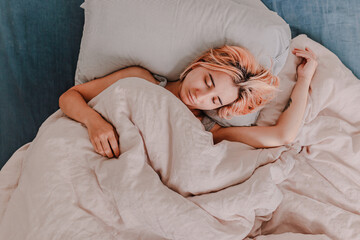 Young woman is relaxing in bed. Day off. Bedtime. Early morning light. White, beige, grey. Light and bright. Morning ritual. Apartment lifestyle living. Cozy bed linen. Taking a nap, sleep. Relaxed