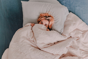 Young woman is relaxing in bed. Day off. Bedtime. Early morning light. White, beige, grey. Light and bright. Morning ritual. Apartment lifestyle living. Cozy bed linen. Taking a nap, sleep. Relaxed