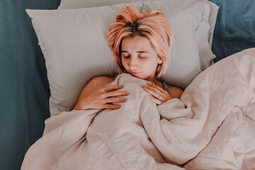 Young woman is relaxing in bed. Day off. Bedtime. Early morning light. White, beige, grey. Light and bright. Morning ritual. Apartment lifestyle living. Cozy bed linen. Taking a nap, sleep. Relaxed