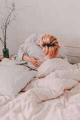 Young woman is relaxing in bed. Day off. Bedtime. Early morning light. White, beige, grey. Light and bright. Morning ritual. Apartment lifestyle living. Cozy bed linen. Soft pillow and comforter.