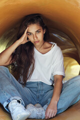 Beautiful stylish girl in jeans and a white T-shirt is sitting with a serious face in a yellow tube. A woman is sitting in a booth at the playground.