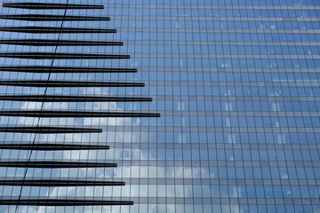 Part of a glass high-rise that reflects the sky with clouds.