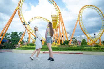 Papier Peint photo Parc dattractions Two cheerful teenage girls enjoy in front of amusement park on weekend.