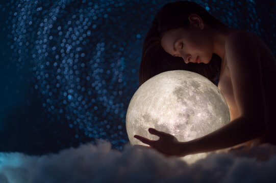 Naked girl with the moon in her hands on a background of stars, femininity and beauty female, clouds, magic and beauty