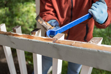 Man Using a Hammer and Pry Bar to Tear Down Old Deck