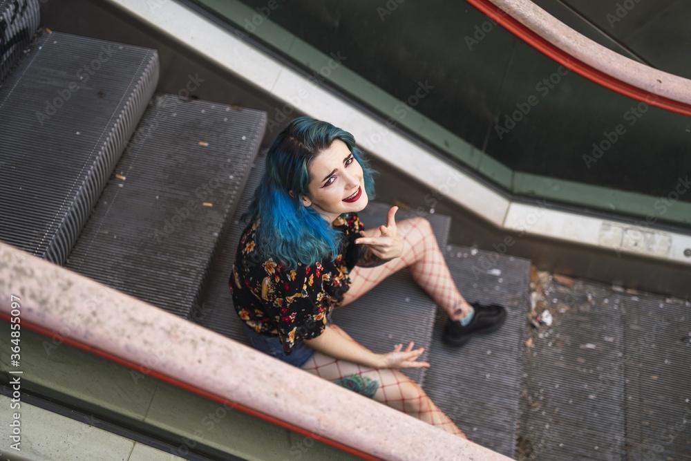 Sticker Beautiful Caucasian female with blue hair posing on an escalator in an old building