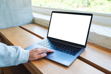 Mockup image of a woman using and touching on laptop computer touchpad with blank white desktop screen on wooden table