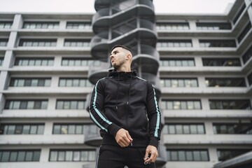 Low angle shot of a Caucasian male with tattoos posing with building in the background © Miguel Angel Junquera/Wirestock