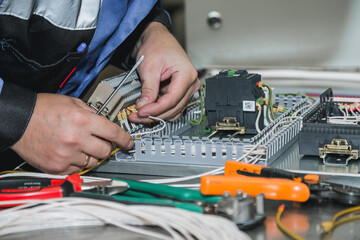 Electrician builder at work inspecting cabling connection of high voltage power electric line in industrial distribution fuseboard. Engineer works with electric cable wires of fuse switch box