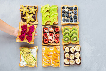 Sandwiches with cream cheese, chocolate, fresh fruits and berries avocado, blueberries, bananas, kiwi, cherry, apricot, dragon fruit on a gray concrete background. top view. Flat lay. Healthy diet