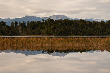 Lake Mahinapua in the South Island of New Zealand on a still day with the trees and mountains reflecting